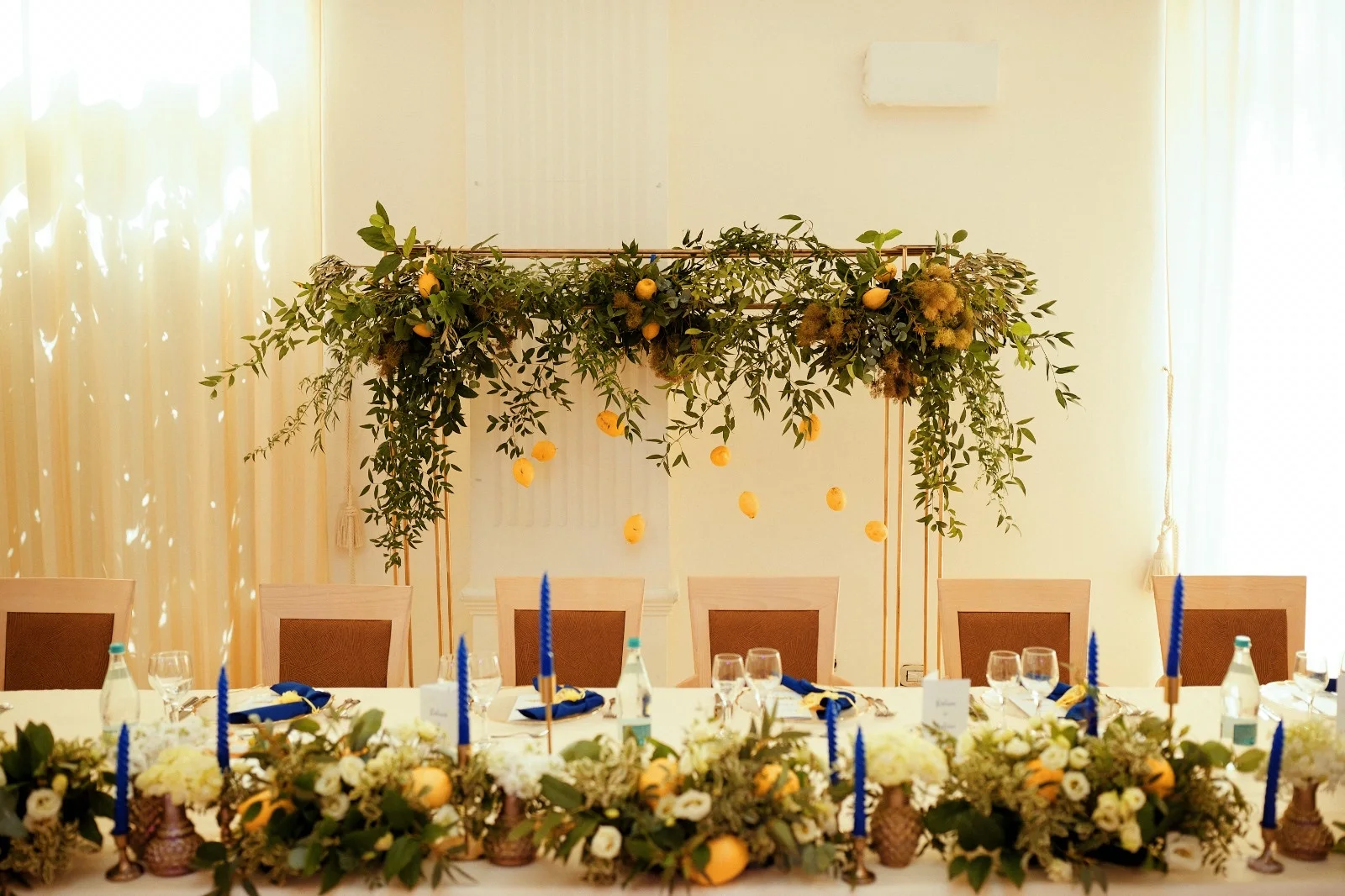 Masă de prezidiu decorată cu verdeață, lămâi și lumânări albastre